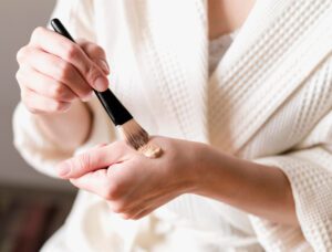 Moteris tepanti makiažo pagrindą ant veido, siekiant natūralaus rezultato